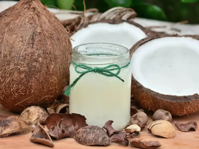 Glas mit Kokosnussöl umgeben von Kokosnüssen