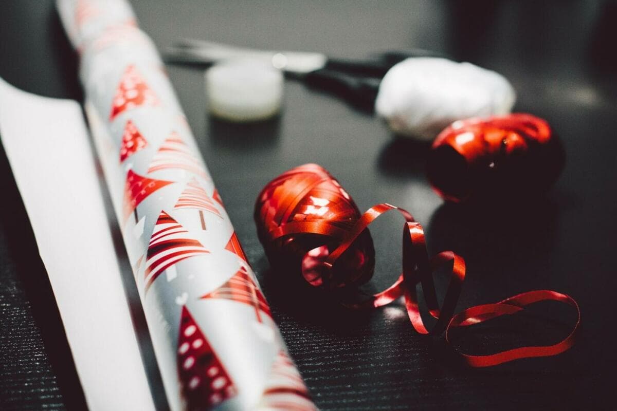 Rot-weißes Geschenkpapier, Geschenkband und schwarze Scheere auf einem Tisch